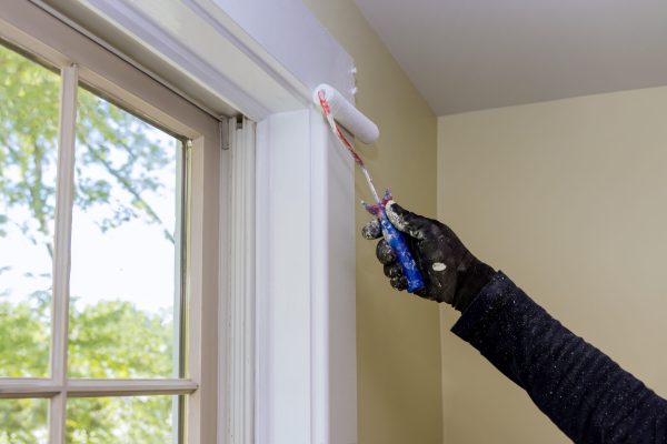 Worker painting using paint roller on layer white color a window frame trim at home renovation